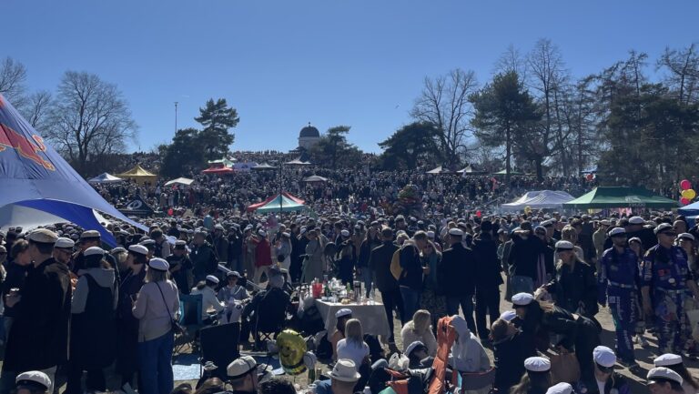 Många människor med vita studentmössor sitter i en solig park.