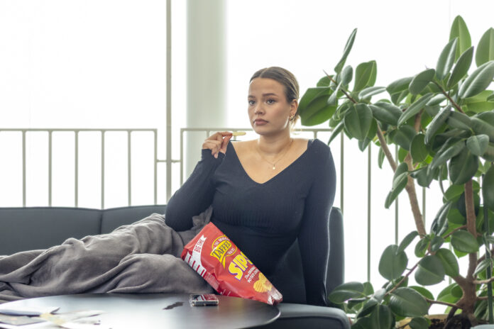 En kvinna ligger på sida i en soffa och äter chips.