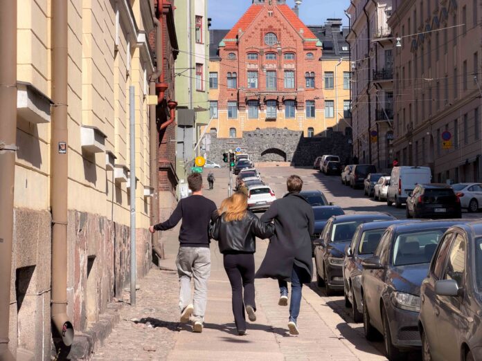 Tre ungdomar som arm i arm skuttar genom Helsingfors soliga gator.