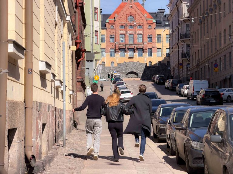 Tre ungdomar som arm i arm skuttar genom Helsingfors soliga gator.