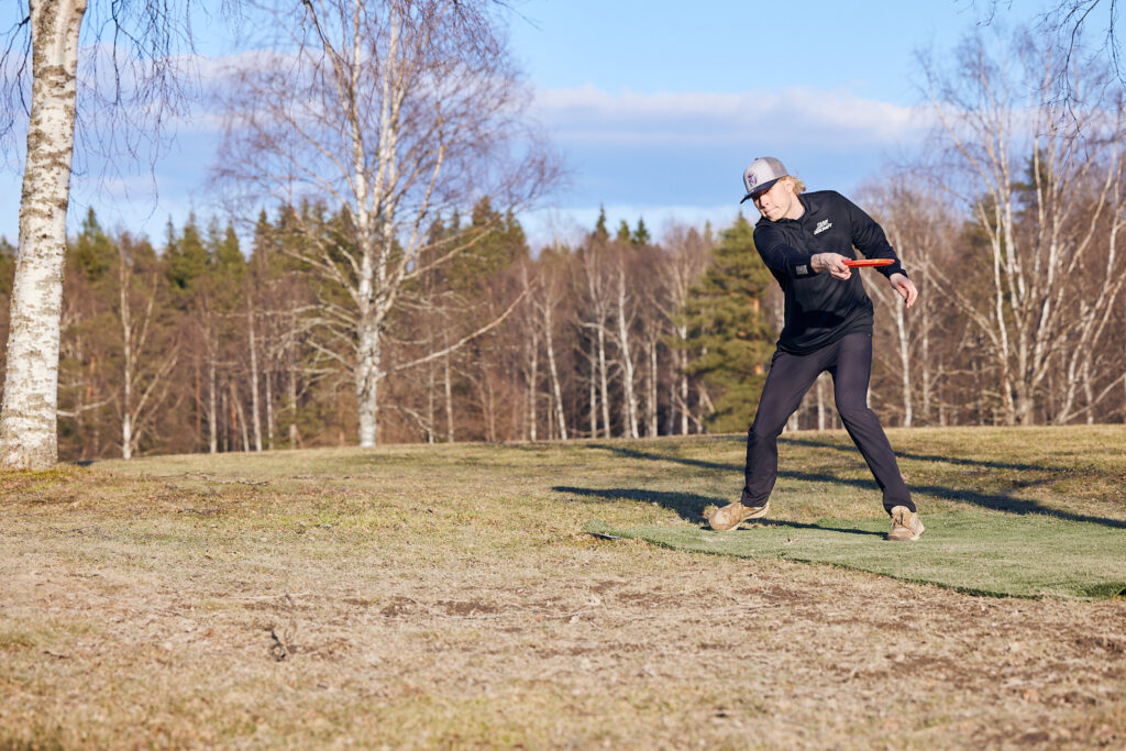 En svartklädd man står på en kulle och kastar en frisbee.