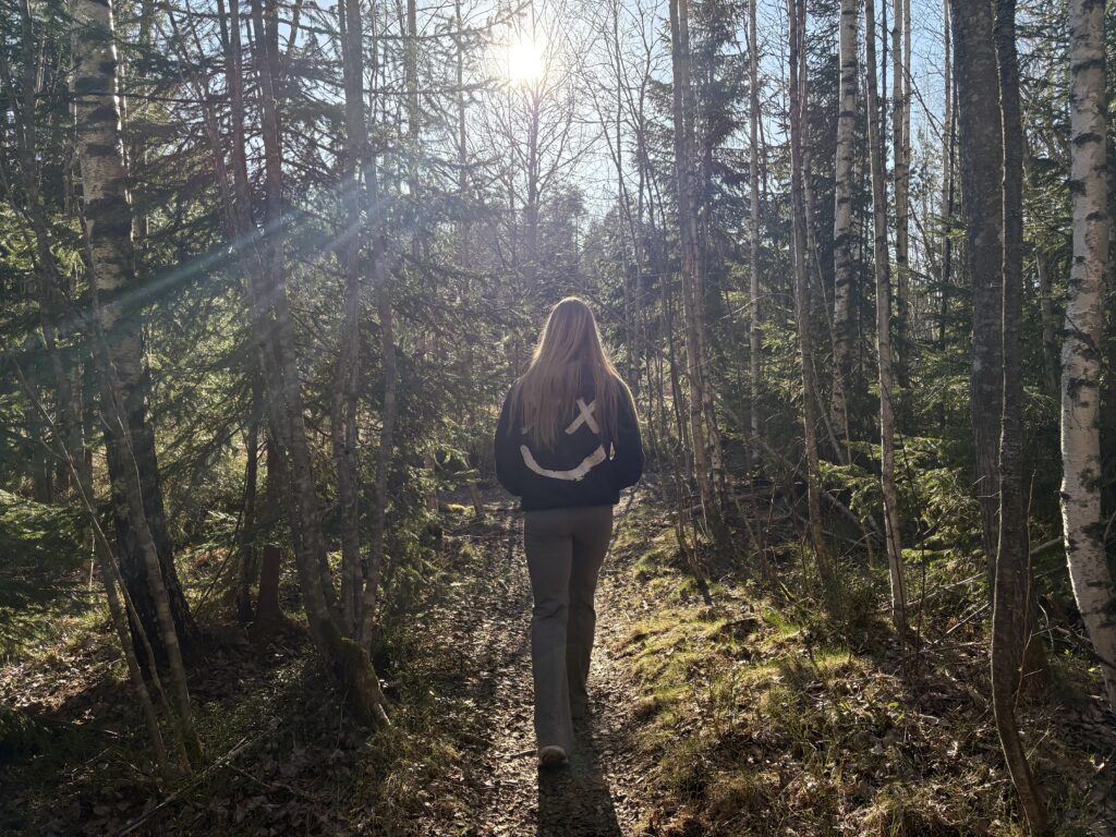 En ung kvinna i svarta kläder går i en solig skog.