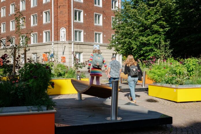 Barn promenerar på sommargatorna i Berghäll bland blomarrangemang